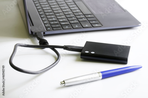 External portable SSD on a white background next to a laptop or ultrabook and a fountain pen. Solid State Drive. The concept of modern gadgets and connecting an SSD drive to a laptop