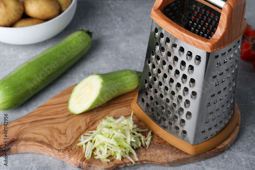 Grater and fresh zucchinis on grey table