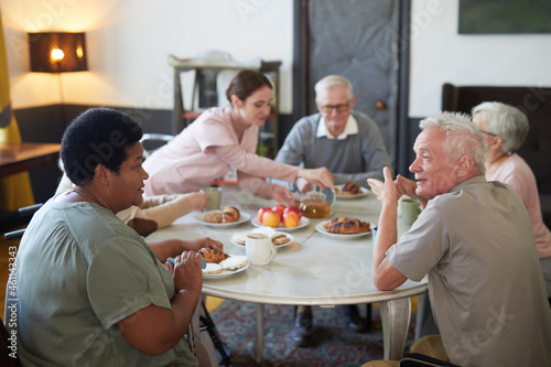 Diverse group of senior people enjoying breakfast at round table in modern nursing home