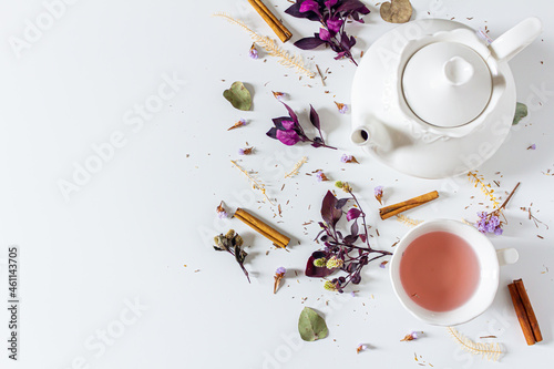 Tea time femine frame composition with tea pot, cinnamon, cup, tea strainer, purple and pink leaves and dried plants  on white background. Flat lay, top view. 