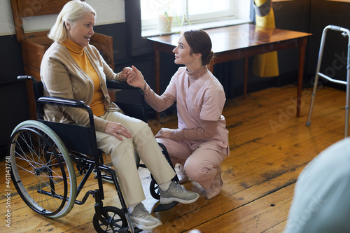 Canvas Print Full length portrait of young woman assisting smiling senior woman in wheelchair