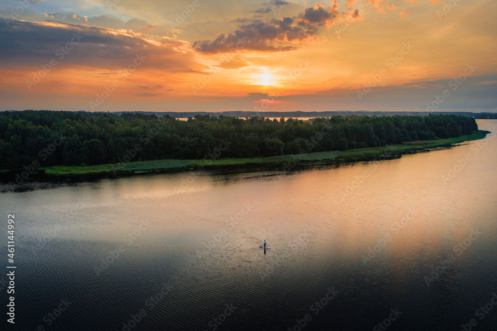 Fototapeta premium Man with stand up paddleboard in water during sunrise