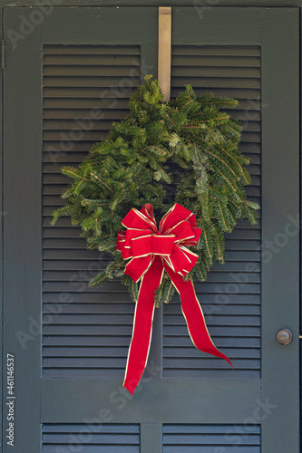Festive fresh green fir holiday wreath with a red bow on a door