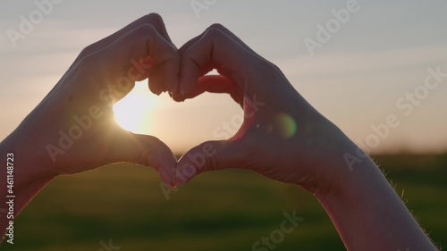 showing with hands heart shape at sunset in the sky, valentine's day, vacation travel concept, weekend, shape with fingers love sign in orange evening light, happy life, romantic mood