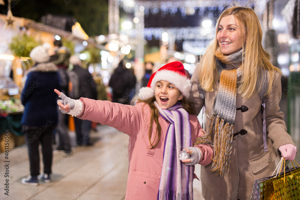 Mom and daughter point to Christmas decorations, choose and buy at the Christmas market