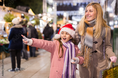 Mom and daughter point to Christmas decorations, choose and buy at the Christmas market