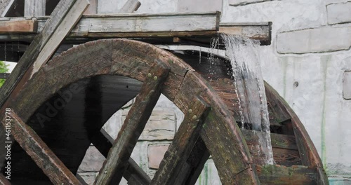 Stream of flowing water turns the wooden wheel of an old water mill.