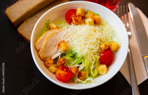 Fresh Caesar salad with chicken served on plate with serving pieces.