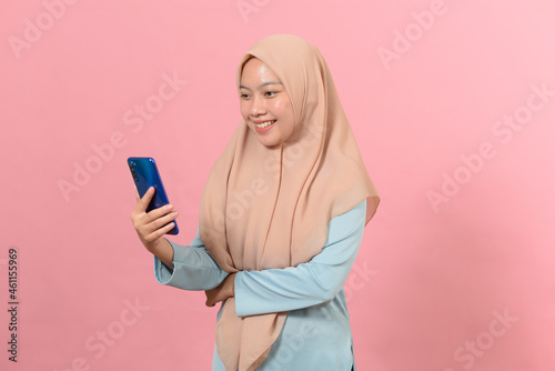 Happy smiling young muslim woman hold smart phone in hands, looking at display screen © Heru