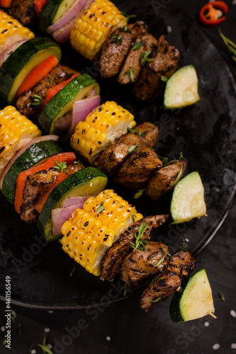 Beef skewers with red onion, green zucchini, red paprika and sweet cob with barbecue salt and thyme on a black background.