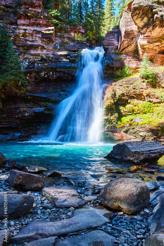 Fototapeta Naklejka Na Ścianę i Meble -  Beautiful waterfall with blue water and large boulders at bottom of canyon