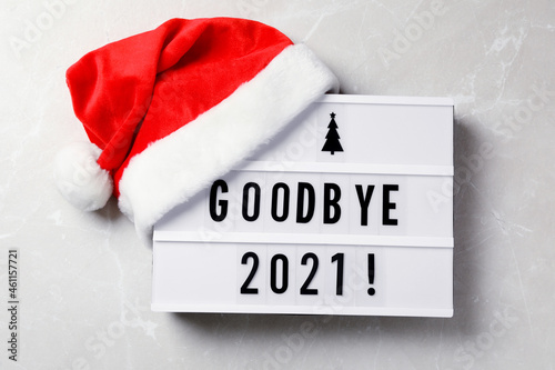 Lightbox with text Bye Bye 2021! and Santa hat on light grey background, flat lay