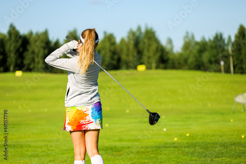 Golfer with a putter on the field. Nearby there is a forest, green grass.