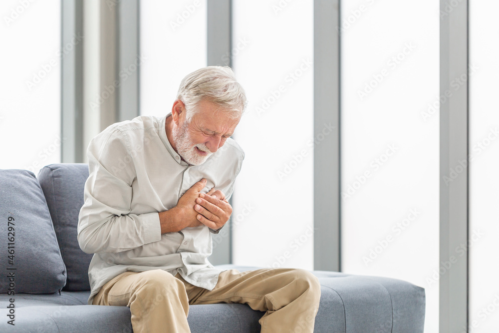 Senior man with pain on heart in living room, Mature man presses hand to chest has heart attack suffers from unbearable pain