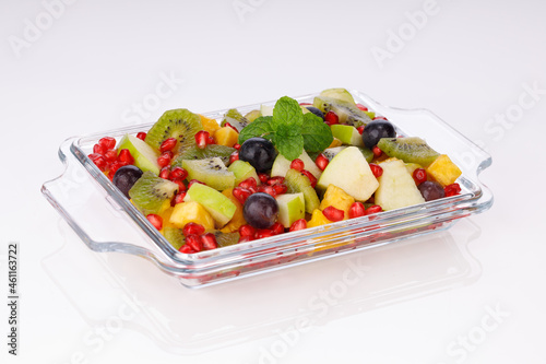 Mixed fruit salad arranged in a transparent rectangle tableware and garnished with mint leaf.