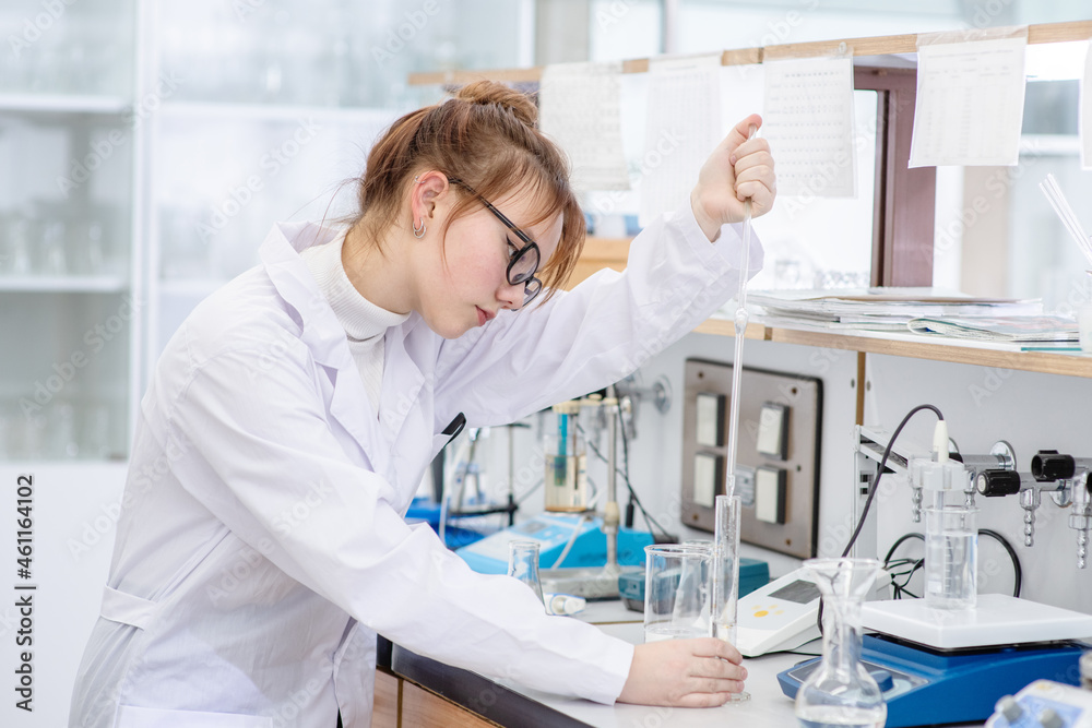 In a chemical laboratory, a girl laboratory assistant drips a solution into a measuring beaker with a special pipette In a chemical laboratory, a girl laboratory assistant drips a solution into a measuring beaker with a special pipette