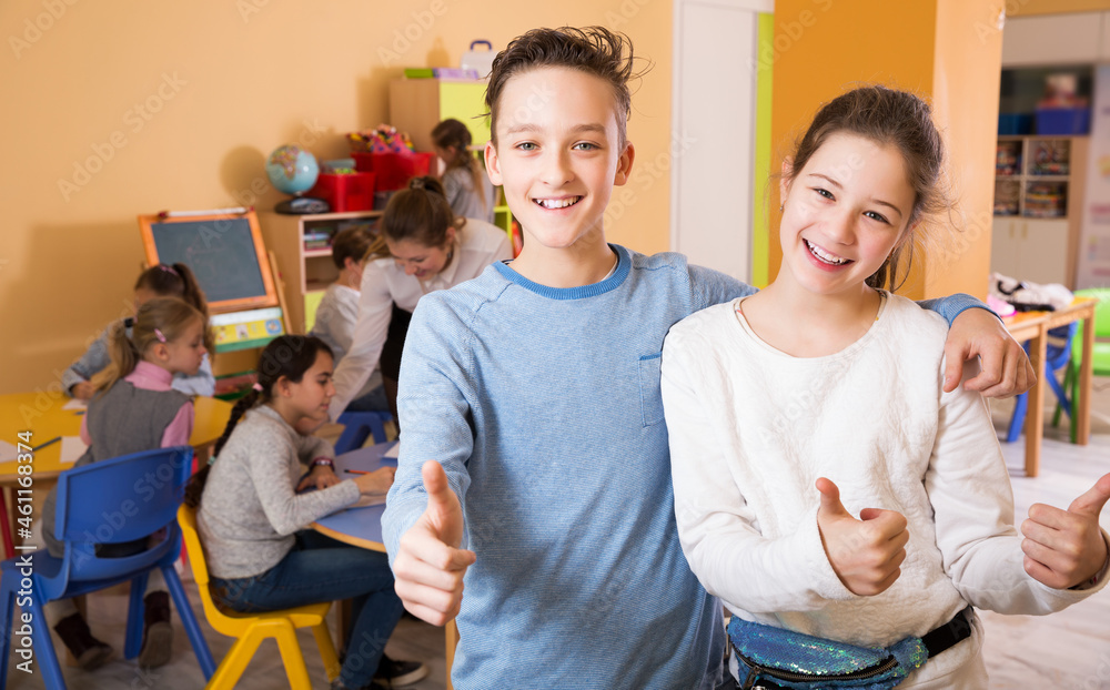 Obraz premium attractive boy and girl holding thumbs up, standing in class with kids
