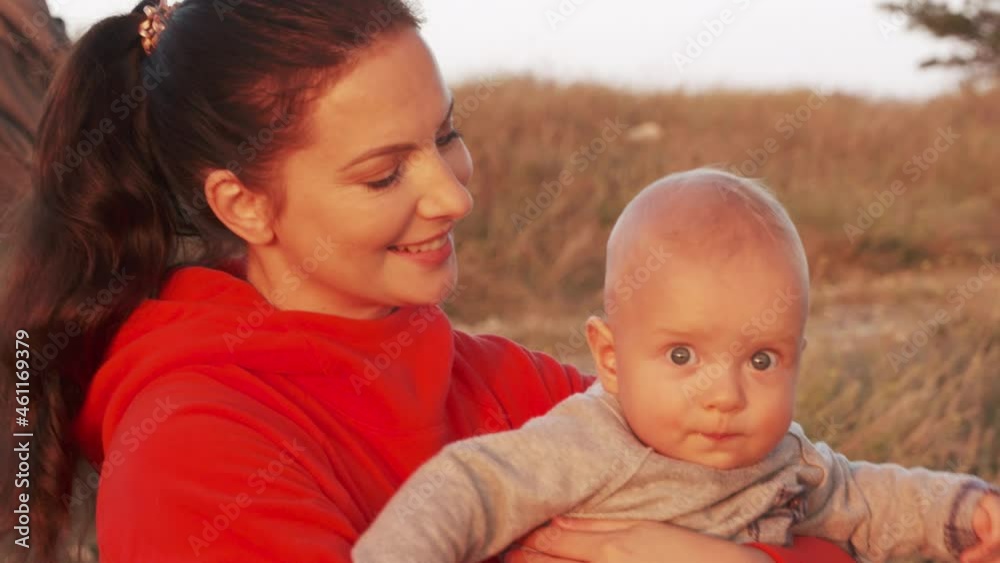 Happy smiling mother with her baby on a walk, portrait of attractive mom with healthy six month old infant against blue sky. High quality 4k footage Happy smiling mother with her baby on a walk, portrait of attractive mom with healthy six month old infant against blue sky. High quality 4k footage