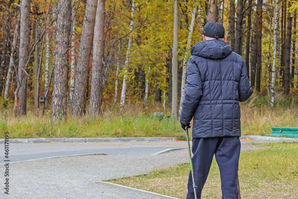A man is engaged in Scandinavian walking in the alley of the park on an autumn day A man is engaged in Scandinavian walking in the alley of the park on an autumn day