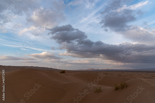 Nature and landscapes of dasht e lut or sahara desert with sand dunes in foreground and cloudy evening sky and mountain in background