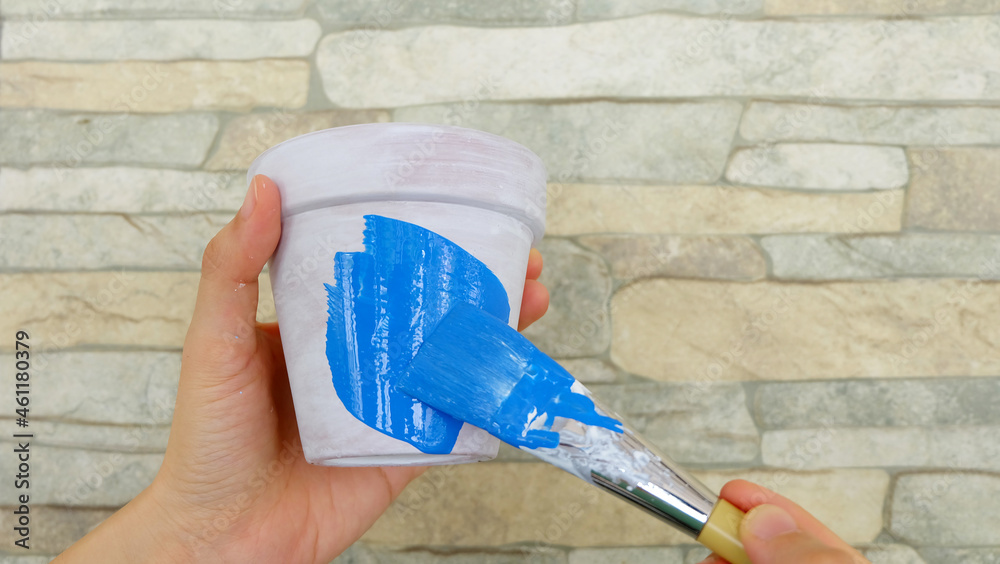 Hand holding a terracotta pot with white base paint, with another hand