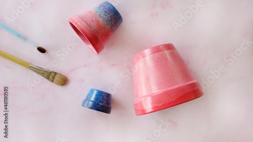Flat lay of pink and blue pots, paint brush and toothbrush. On a pink surface.