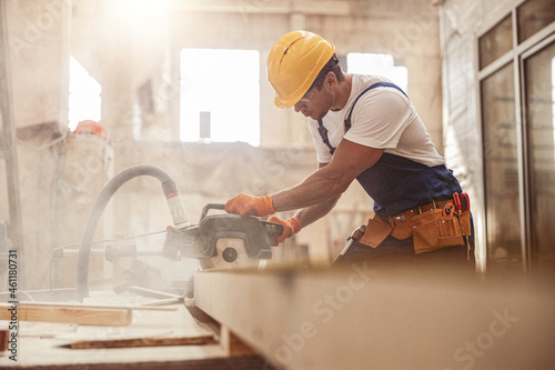 Male builder using wood cutting circular saw machine in workshop photo