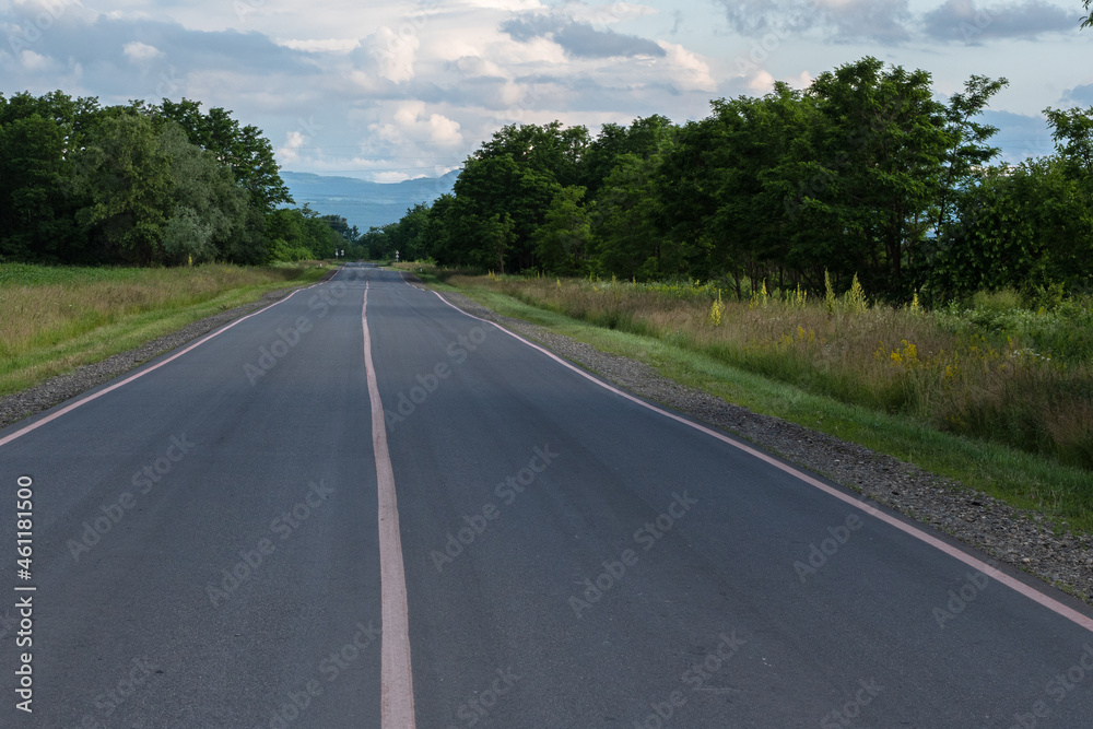 A suburban asphalt road with three solid lines of pink road markings. In the background of the mountain and the blue sky with clouds. The concept of travel. A suburban asphalt road with three solid lines of pink road markings. In the background of the mountain and the blue sky with clouds. The concept of travel.