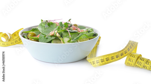 Plate with healthy salad and measuring tape on white background