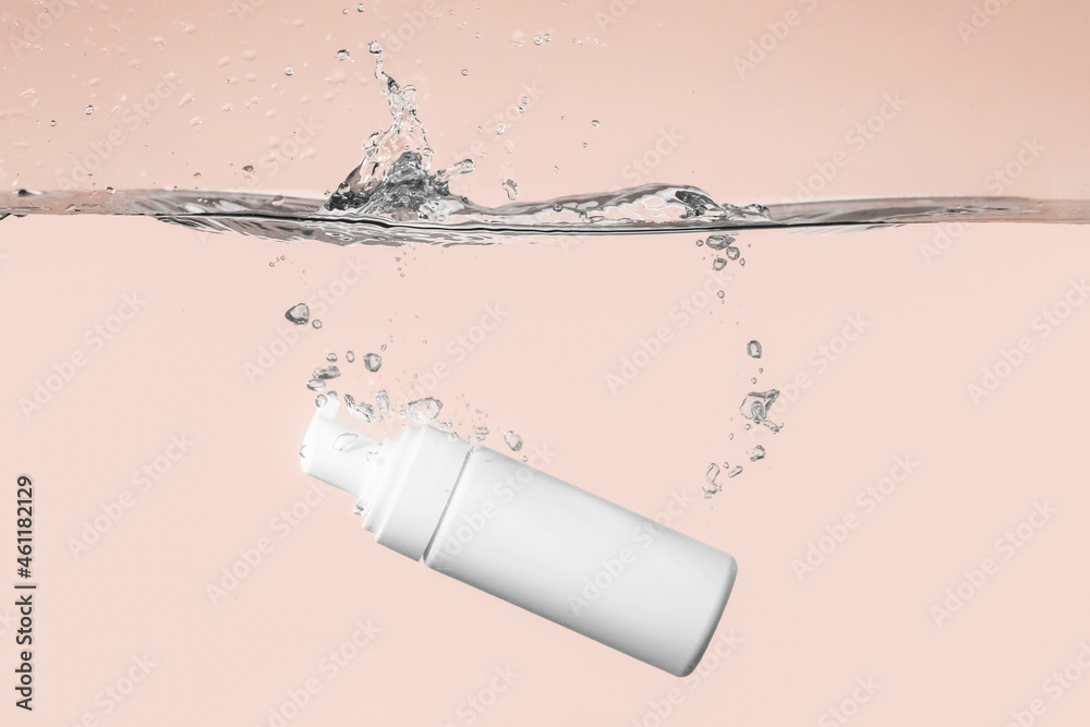 Bottle of cosmetic product in water with splashes on color background - obrazy, fototapety, plakaty 