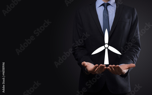 Businessman holding an icon of a windmill that produces environmental energy. Dark background