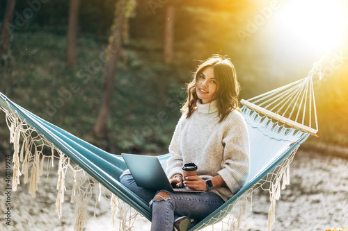 Beautiful smiling girl working on laptop in the park on a hammock © alimyakubov