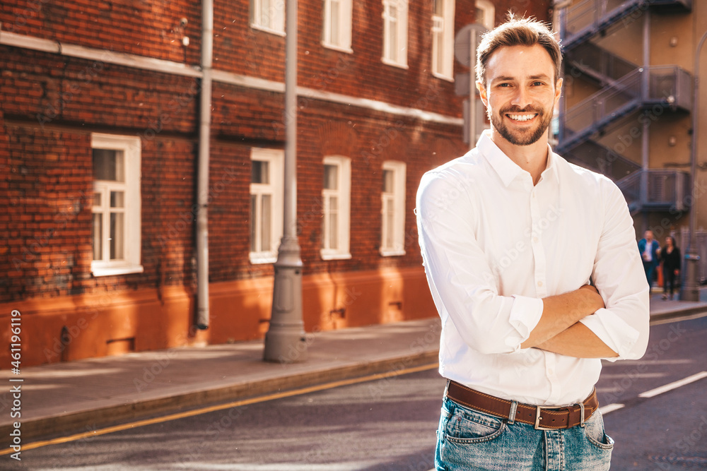 Fototapeta premium Portrait of handsome smiling stylish hipster lambersexual model.Modern man dressed in white shirt. Fashion male posing on the street background. Outdoors at sunset