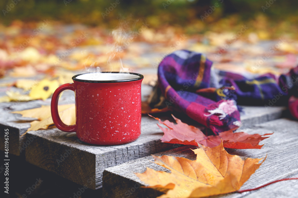 Autumn coffee or tea in a cup on a wooden table against the background of yellow fallen leaves and October weather. Autumn drink, mood and comfort concept. - obrazy, fototapety, plakaty 