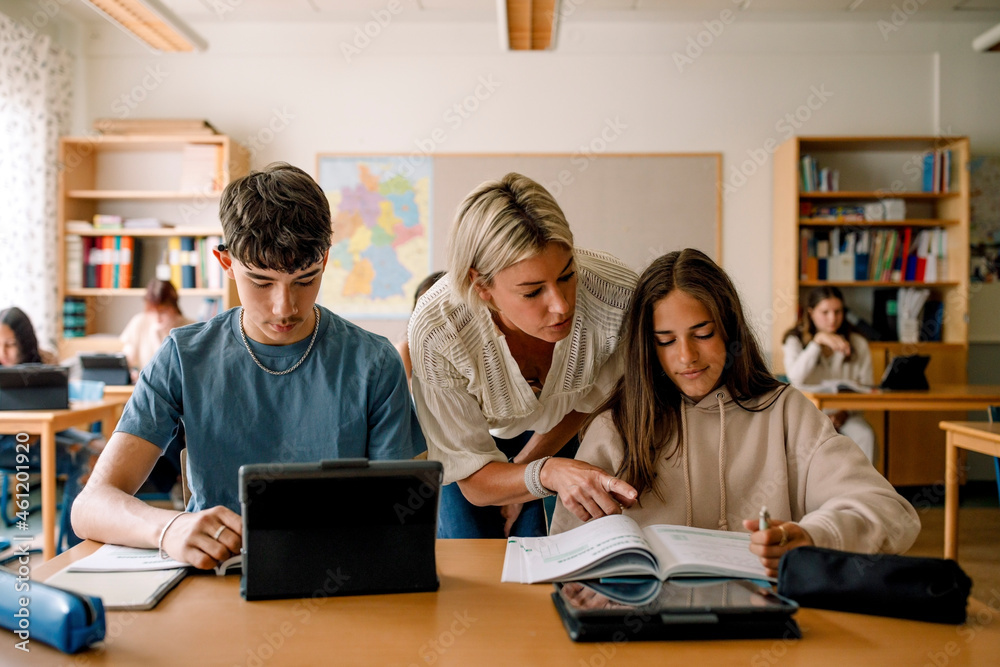 Female teacher teaching teenage girl on book in classroom Female teacher teaching teenage girl on book in classroom