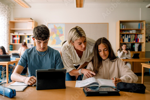 Female teacher teaching teenage girl on book in classroom photo
