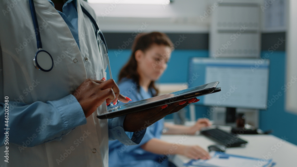 Close up of african american doctor using tablet with touch screen for healthcare information in cabinet. Black medic with white coat and stethoscope holding modern gadget for medical care