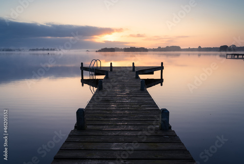 An empty jetty in a lake during a tranquil  foggy dawn.