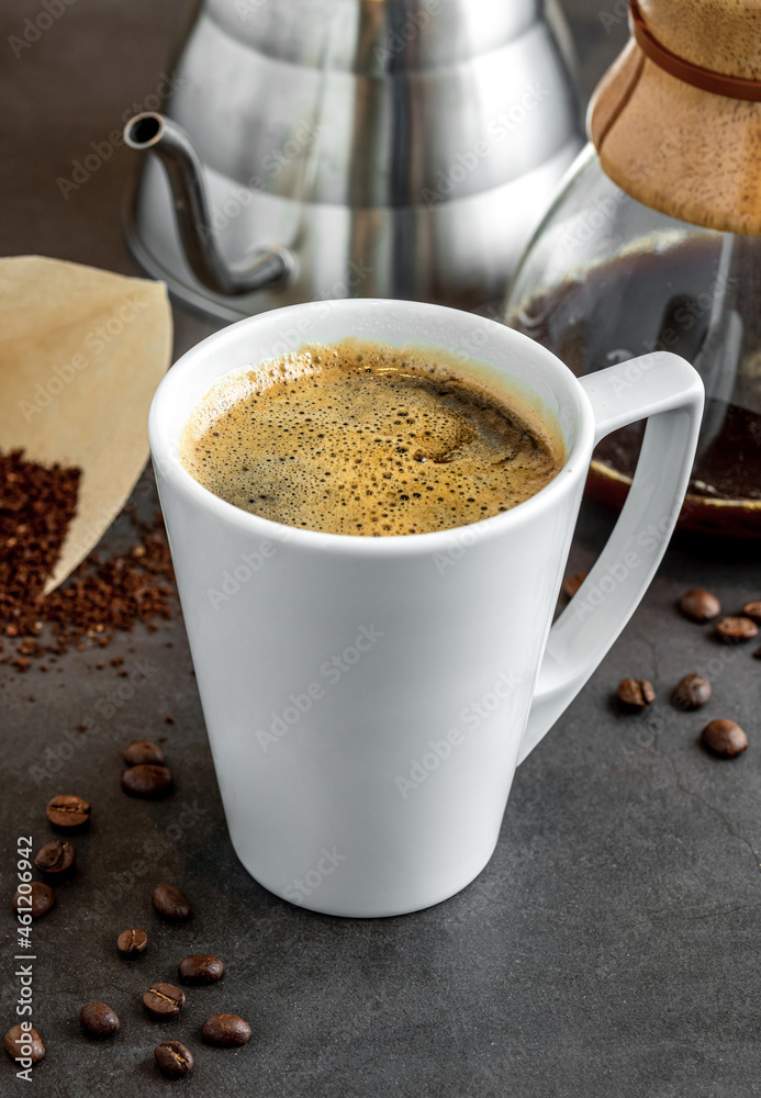 A cup of coffee and third generation pour over coffee brewing equipment on stone floor