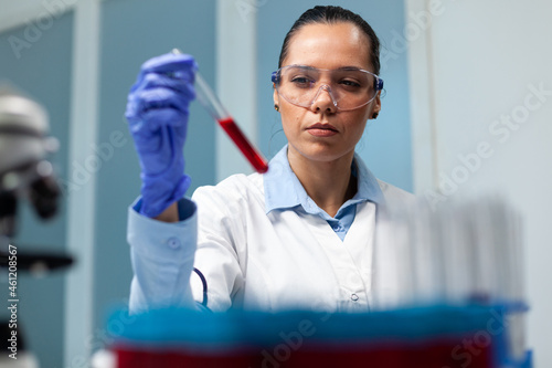 Scientist woman holding blood test tube working at microbiology experiment in medicine biochemistry laboratory. Specialist doctor analyzing disease discovering medical healthcare treatment photo