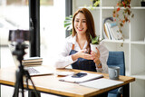 Young Asian women blogger showing clothes in front of the camera to recording vlog video live streaming at her shop. Network technology Business online influencer on social media concept.