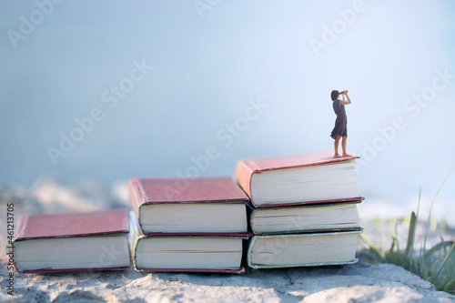 woman with binoculars on the top of a ladder of books, surreal concept