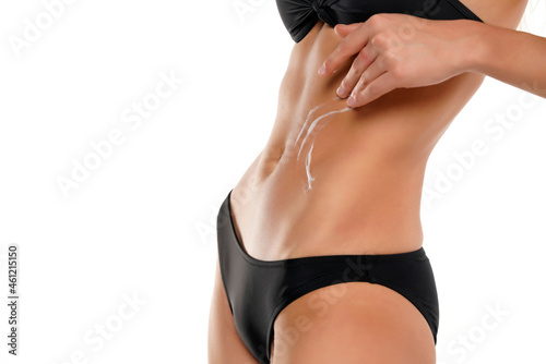 Young slim woman applying cosmetic product on her belly