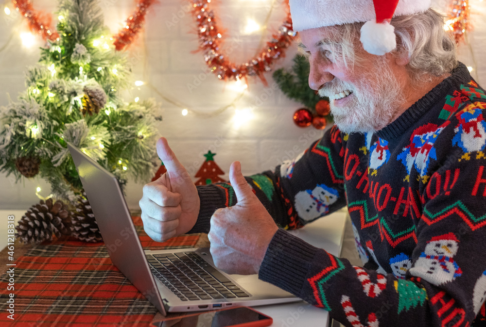 Fototapeta premium Old senior man happy in video call from home at Christmas. Using laptop gesturing optimistic smiling beard new year