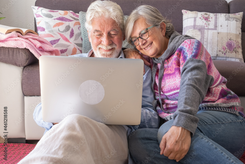 Attractive senior couple at home using together same laptop. Smiling elderly retiree enjoying free time,  technology and social media