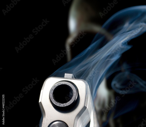 3D rendering with a smoking semi automatic pistol in front of a slightly out of focus skull behind representing a ghost gun