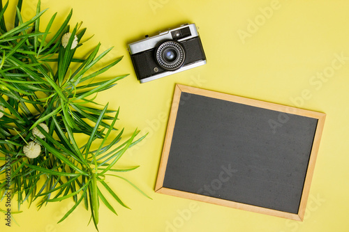 A cemera with leaves and blackboard over the yellow background.  photo