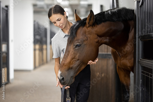 Bild auf Leinwand Side view of female horseman feeding her brown Thoroughbred horse in stable