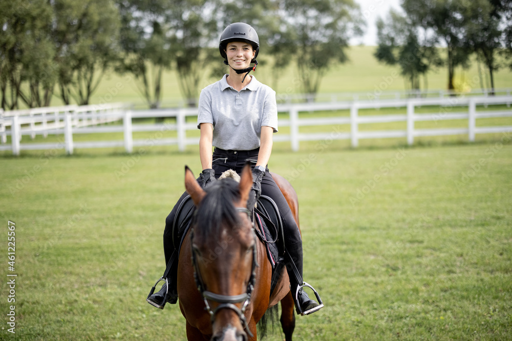 Female horseman riding brown Thoroughbred horse on green meadow in countryside. Concept of rural resting and leisure. Green tourism. Young smiling european woman. Beautiful landscape at sunny day Female horseman riding brown Thoroughbred horse on green meadow in countryside. Concept of rural resting and leisure. Green tourism. Young smiling european woman. Beautiful landscape at sunny day