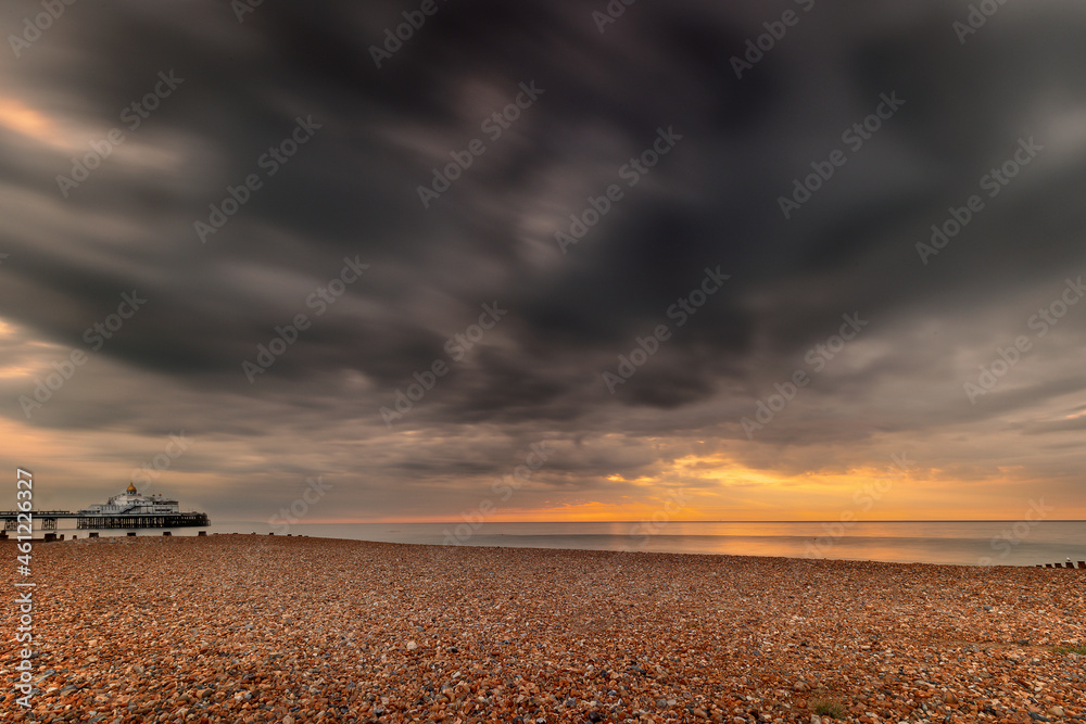 Fototapeta premium Landscape orientation shot of a sunrise in Eastbourne, East Sussex, United Kingdom, long exposure shot showing movement of clouds and dramatic skies and the pier, wide angle shots,